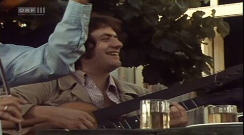 Standbild aus einer Fernsehaufnahme des ORF von 1974, gezeigt auf ORF III: Harry Pepl lachend mit der Gitarre beim Heurigen. Nach Angaben der Familie eine seltene Aufnahme mit dem Maler und Sänger Arik Brauer, Pepl ist ab etwa Minute 4 zu sehen; Titel und Erstsendedatum der Sendung werden noch ermittelt. Kleines Bildzitat als Hinweis auf die Sendung.
