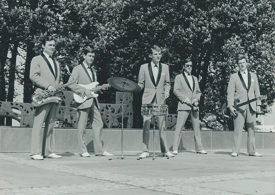 Schwarzweißfoto der Austrian Evergreens, mit denen Pepl 1962 und 1964 Singles aufnahm: fünf Musiker in hellen Anzügen mit dunklem Revers stehen auf einem Platz, mit Saxofon, zwei Gitarren und Schlagzeug, dahinter Bäume; Harry Pepl mit Gitarre.