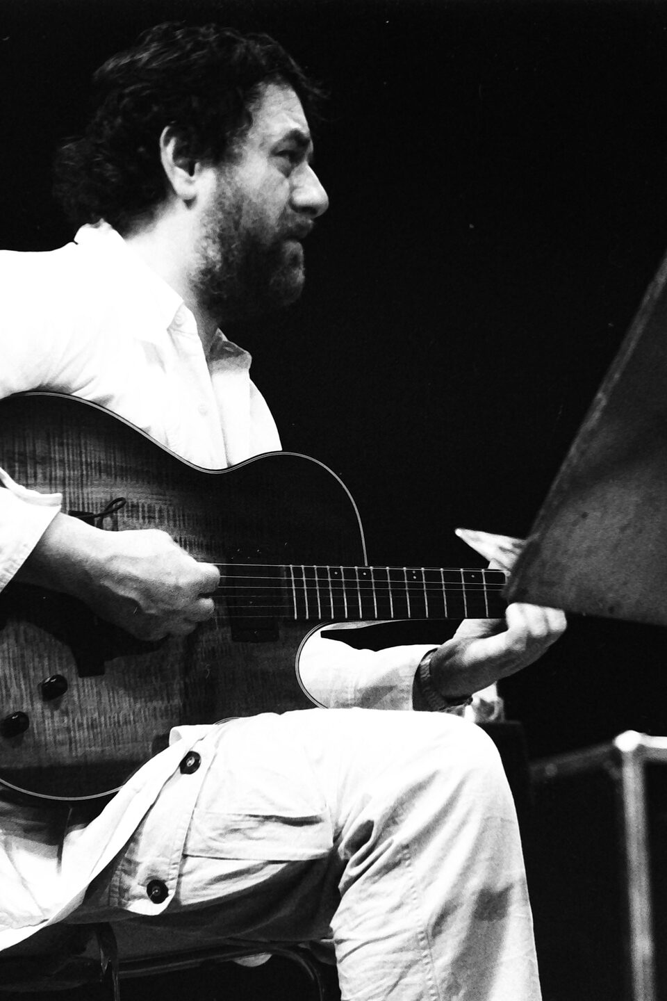 Harry Pepl sitzend mit der Archtop-Gitarre auf der Bühne des Jazzfestivals Amiens, Frankreich, im Mai 1987, im Profil, der Blick geht zum Notenpult.