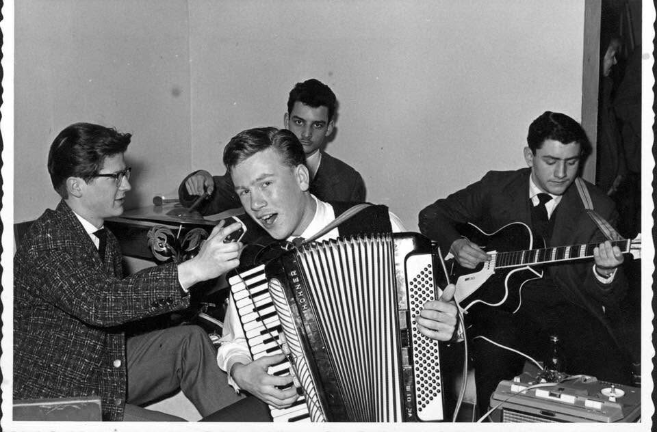 Schwarzweißfoto mit Büttenrand: vier junge Musiker mit Akkordeon, Schlagzeug und E-Gitarre, an der Gitarre rechts vermutlich Harry Pepl, vorne ein Tonbandgerät. Laut Beschriftung der Familie spielen Blacky Brandstätter, Franz Handler, Karl Komarek und Harry Pepl; welcher Name zu welchem Musiker gehört, ist noch offen.